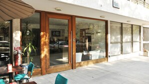 Un espacio exterior con mesas y sillas, un hidrante y la entrada de un edificio con puertas de cristal.