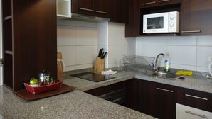 Una cocina moderna con armarios de madera oscura, encimera de granito, microondas integrado y pileta de acero inoxidable.