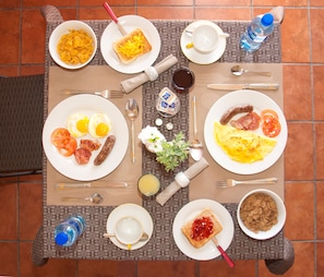 Une table mise pour le petit-déjeuner avec des assiettes d’œufs, des toasts et des saucisses, ainsi qu’un bol de céréales et une bouteille d’eau.