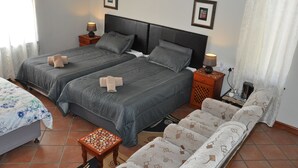 Ein Hotelzimmer mit zwei Betten, einem Schlafsofa, einem kleinen Tisch und einem Nachttisch mit Lampe.