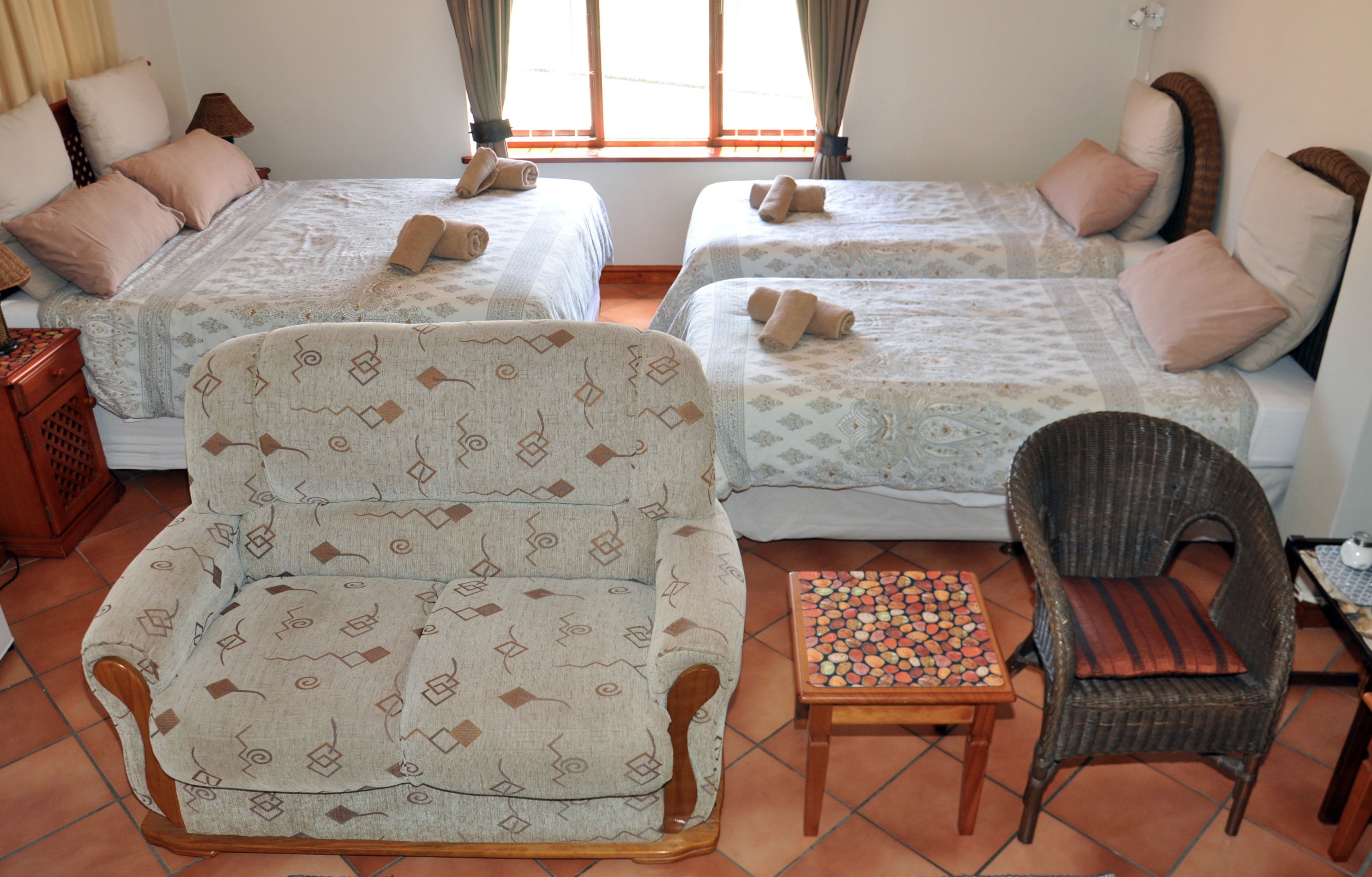 A room with two beds, a chair, a small table, and a wicker chair.
