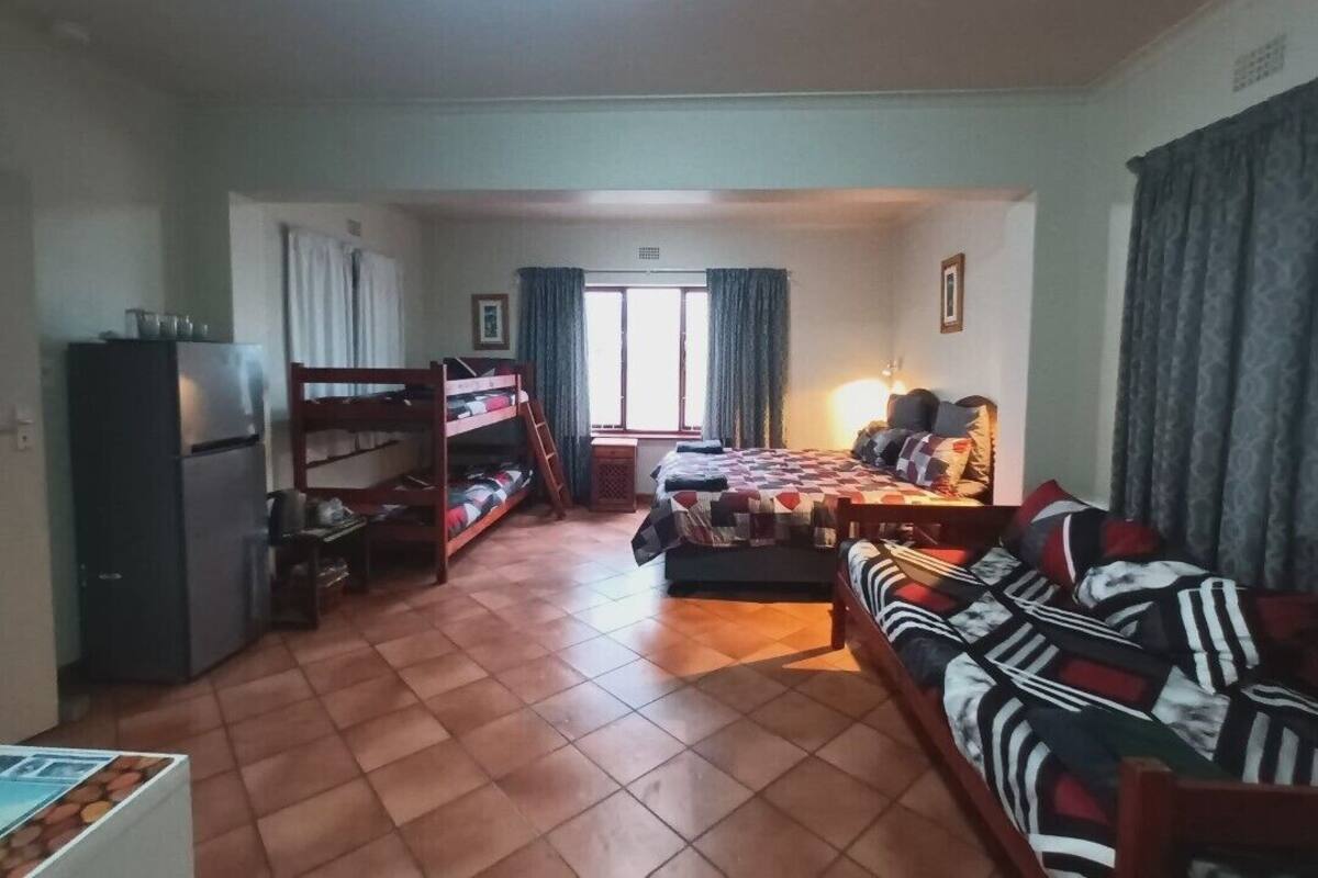 A compact living space with a kitchenette, a bed with a patterned bedspread, a sofa, and a window with curtains.