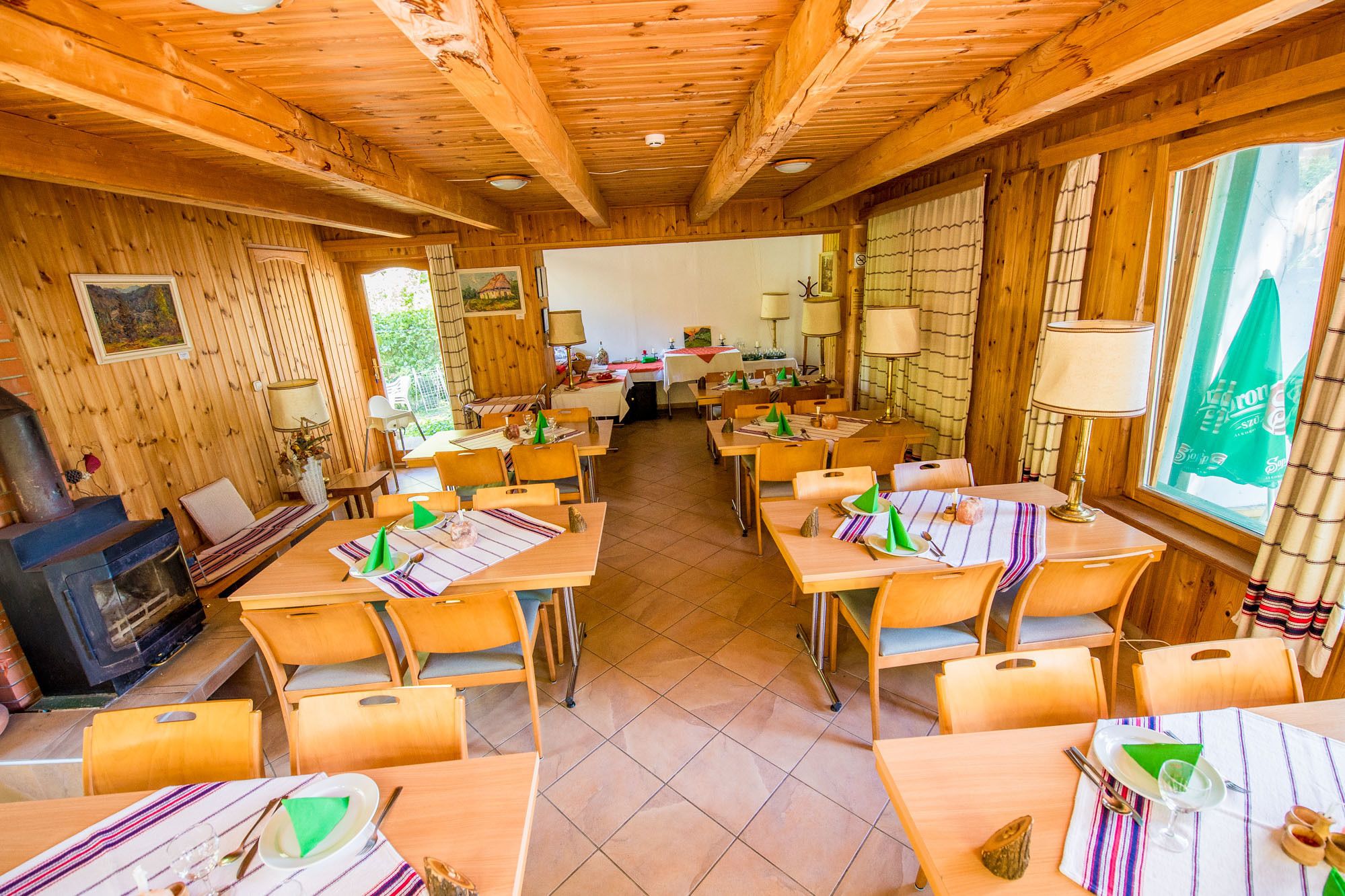 A wooden interior with multiple dining tables and chairs, a fireplace, and large windows.