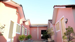 A pink building with a tiled roof, stone pathway, and potted plants. - Pousada LN (Caldas Novas)