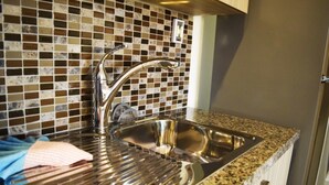 Uma cozinha com uma pia de aço inoxidável, painel de azulejos e bancada de granito.