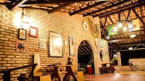 An indoor space with brick walls, wooden tables, and chairs. There are framed pictures on the walls and a Brazilian flag. - Oh Linda Pousada (Icapuí)