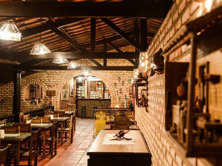 Un restaurante con paredes de ladrillo, vigas de madera y lámparas colgantes. Mesas y sillas dispuestas para comer.