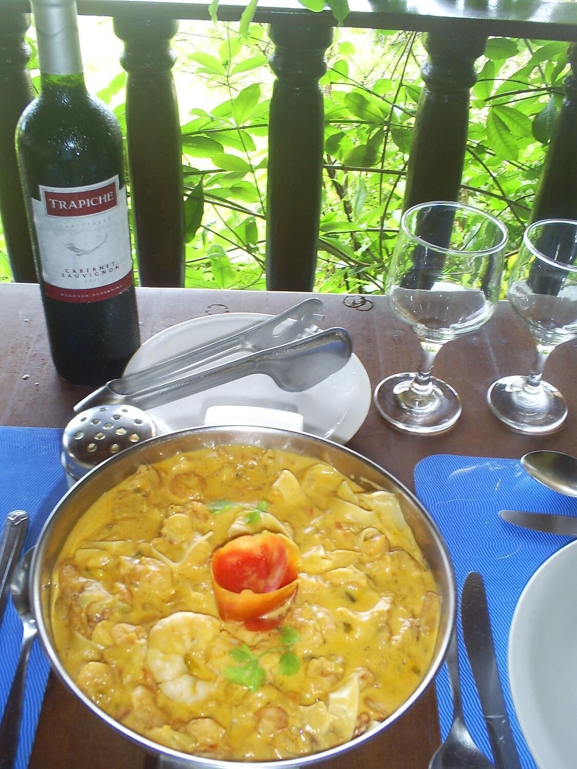 A table with a bowl of seafood curry, a bottle of wine, and empty wine glasses.
