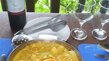 A table with a bowl of seafood curry, a bottle of wine, and empty wine glasses.