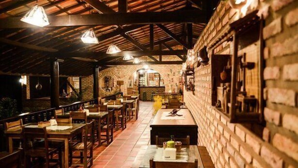 A restaurant with brick walls, wooden tables and chairs, and hanging pendant lights. - Oh Linda Pousada (Icapuí)
