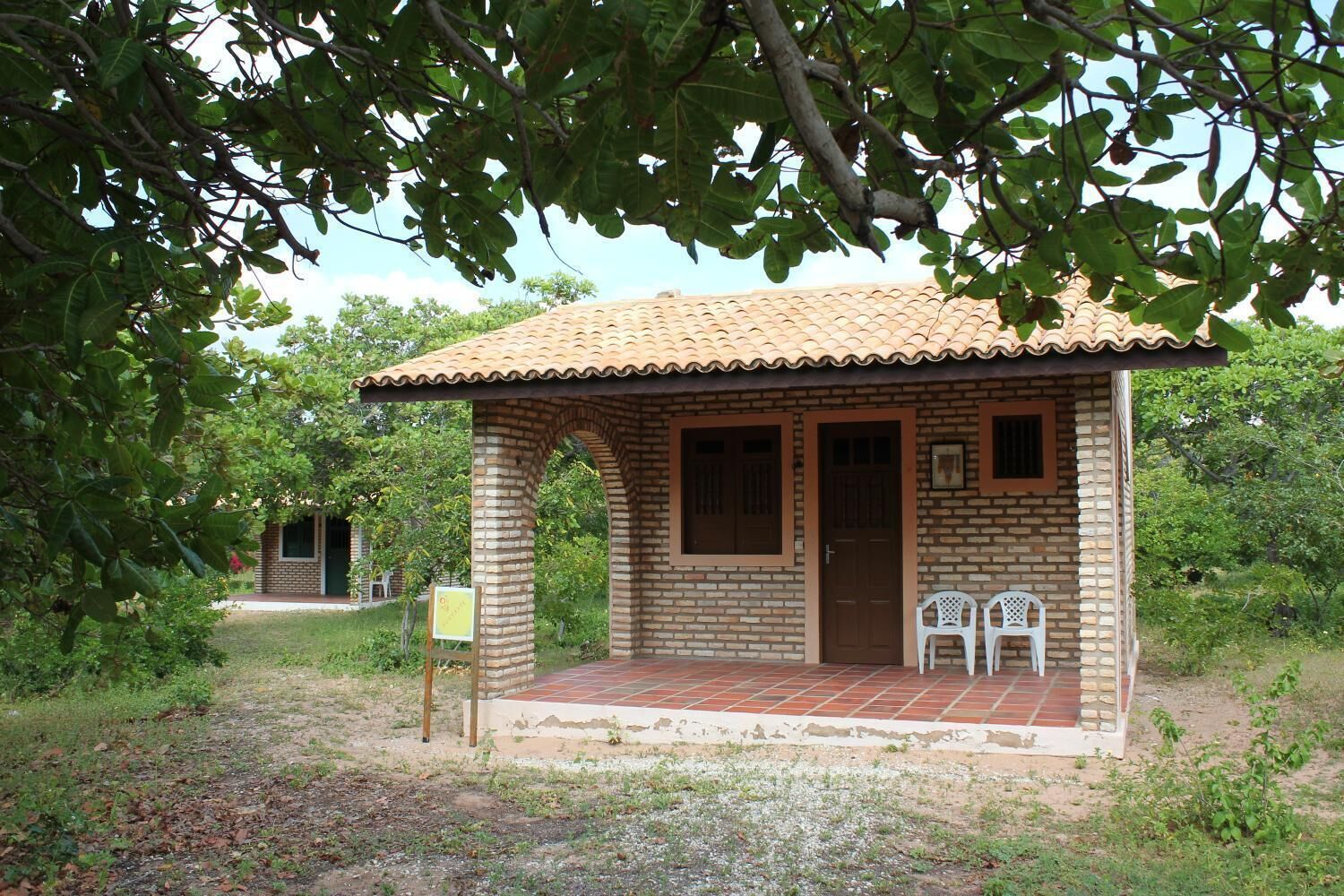 Une petite maison en briques avec un toit en tuiles, une porte et deux chaises en plastique blanches devant.