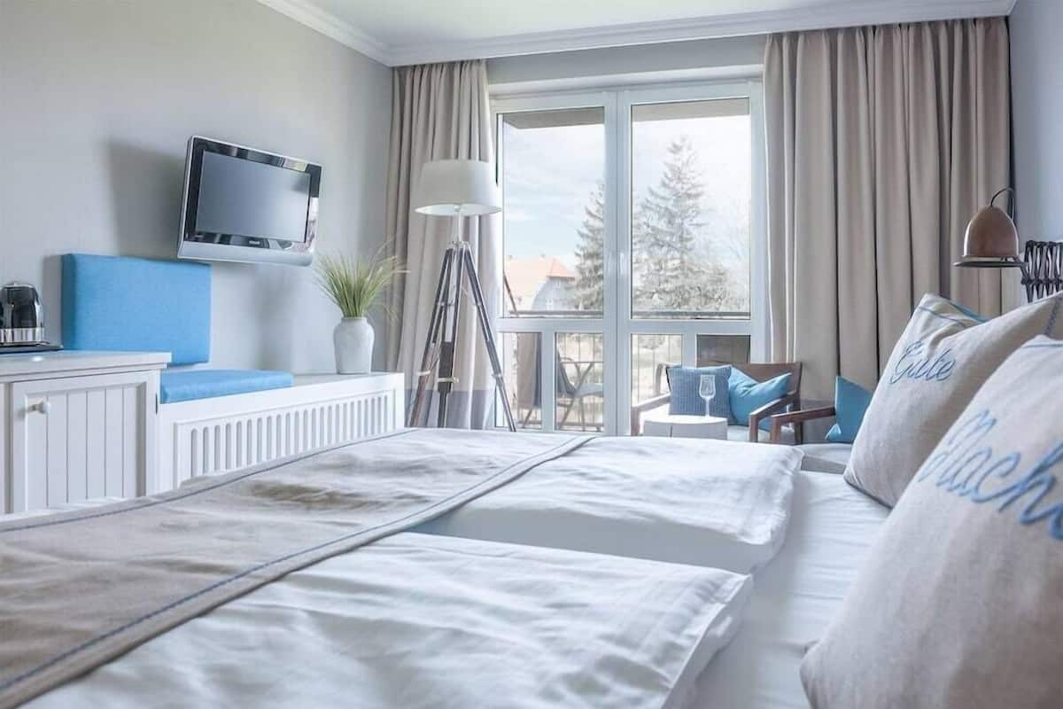 Hotelkamer met een bed, een televisie, een bureau, een stoel, een lamp en uitzicht op bomen door het raam.