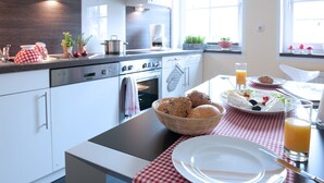 Een moderne keuken met witte kastjes, een roestvrijstalen fornuis en een eethoek met een geruit tafelkleed.