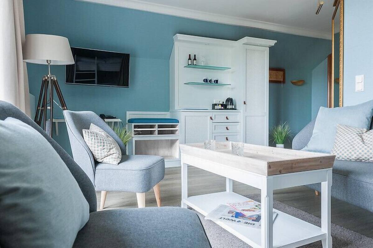 Een moderne woonkamer met een blauwe wand, een witte kast met glazen planken, een vloerlamp en een salontafel.