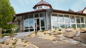 Een modern gebouw met een grote glazen gevel, een opvallend rood dak en een houten terras ervoor.