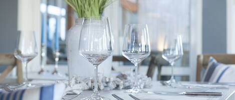A dining table set with wine glasses, cutlery, and a decorative vase with green plants.