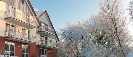A multi-story residential building with balconies, a brick facade, and a snow-covered landscape.