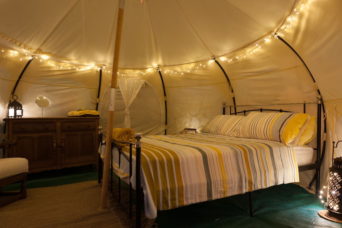 A tent with a bed, bedside table, lamp, and string lights.