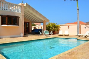 Une piscine avec des chaises longues et un espace patio couvert.