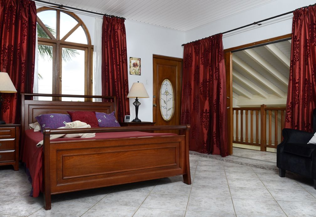 A bedroom with a wooden bed, red curtains, a clock on the wall, and a view of the outside.
