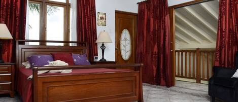 A bedroom with a wooden bed, red curtains, a clock on the wall, and a view of the outside.