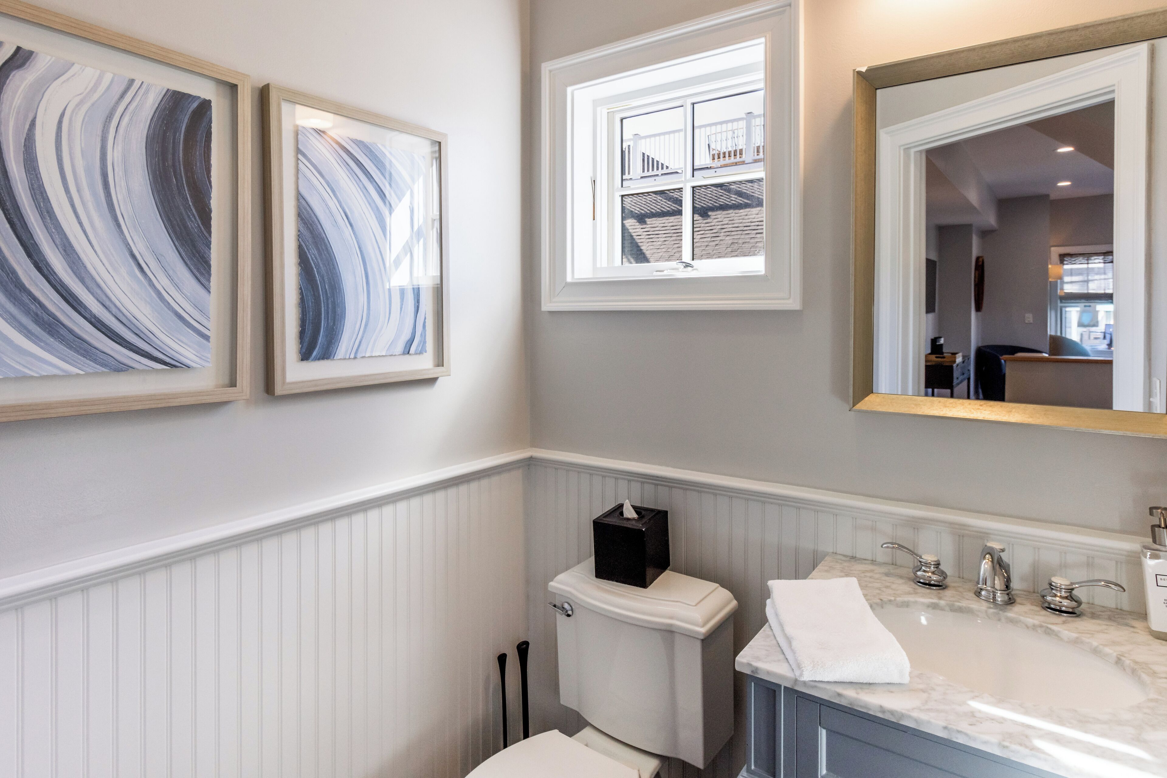A bathroom with a white toilet, a sink with a marble countertop, and two framed artworks on the wall.
