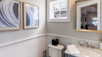 A bathroom with a white toilet, a sink with a marble countertop, and two framed artworks on the wall.