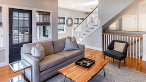 A modern living room with a gray sofa, a wooden coffee table, and a staircase leading to a second floor. - The Newport Lofts - 595 Thames Street (Newport)
