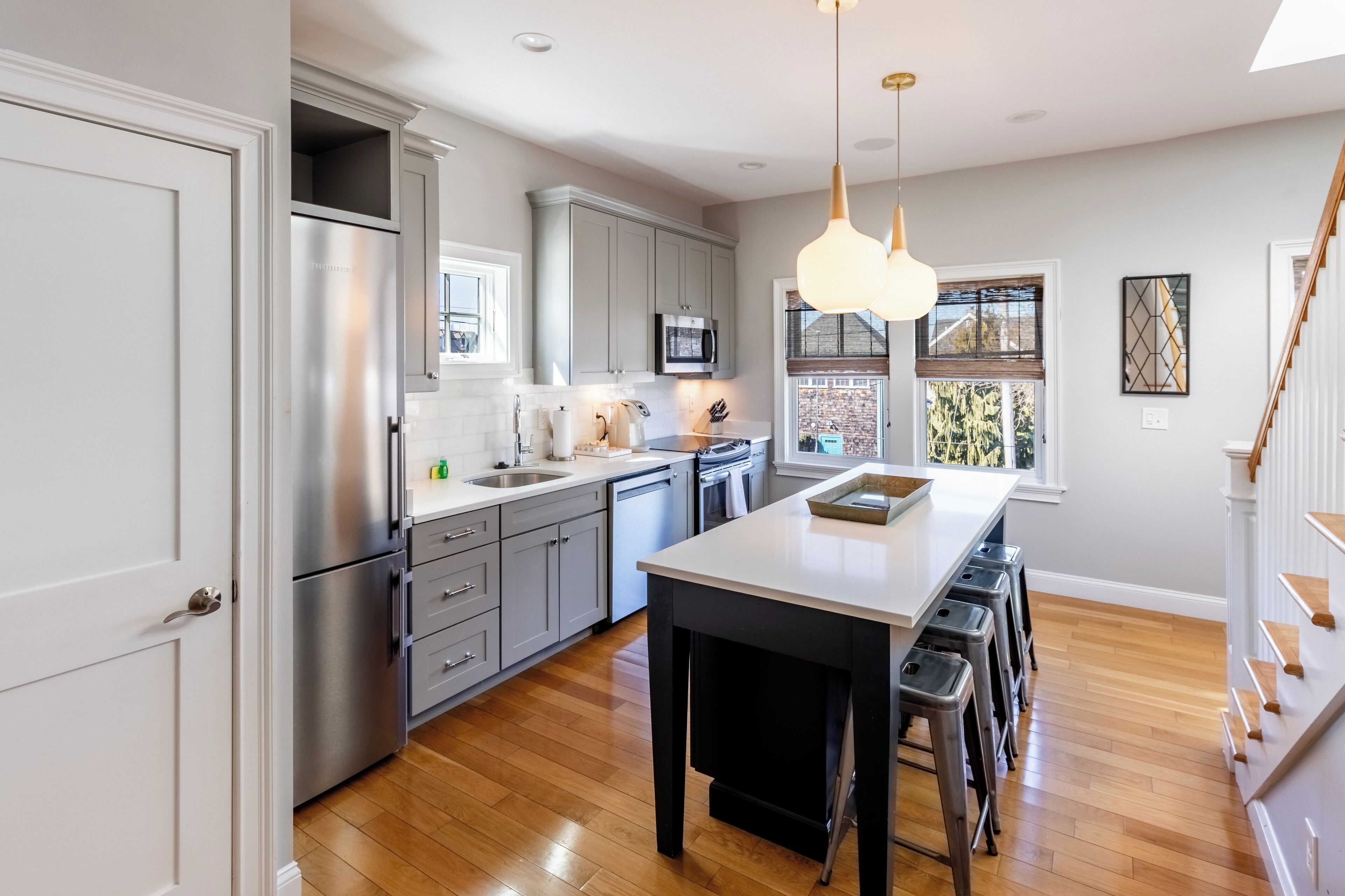 A modern kitchen with stainless steel appliances, a central island, and a view of the outdoors through large windows.