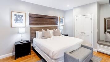 Quarto moderno com cama grande, mesa de cabeceira, banqueta e guarda-roupa.