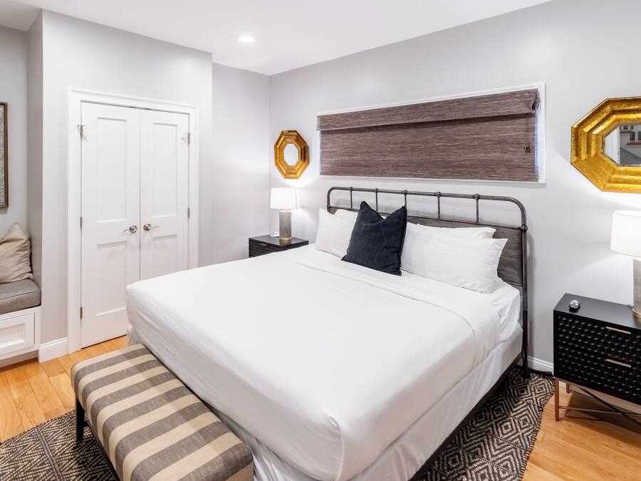 A modern bedroom with a large bed, bedside tables, a bench, and a wardrobe.