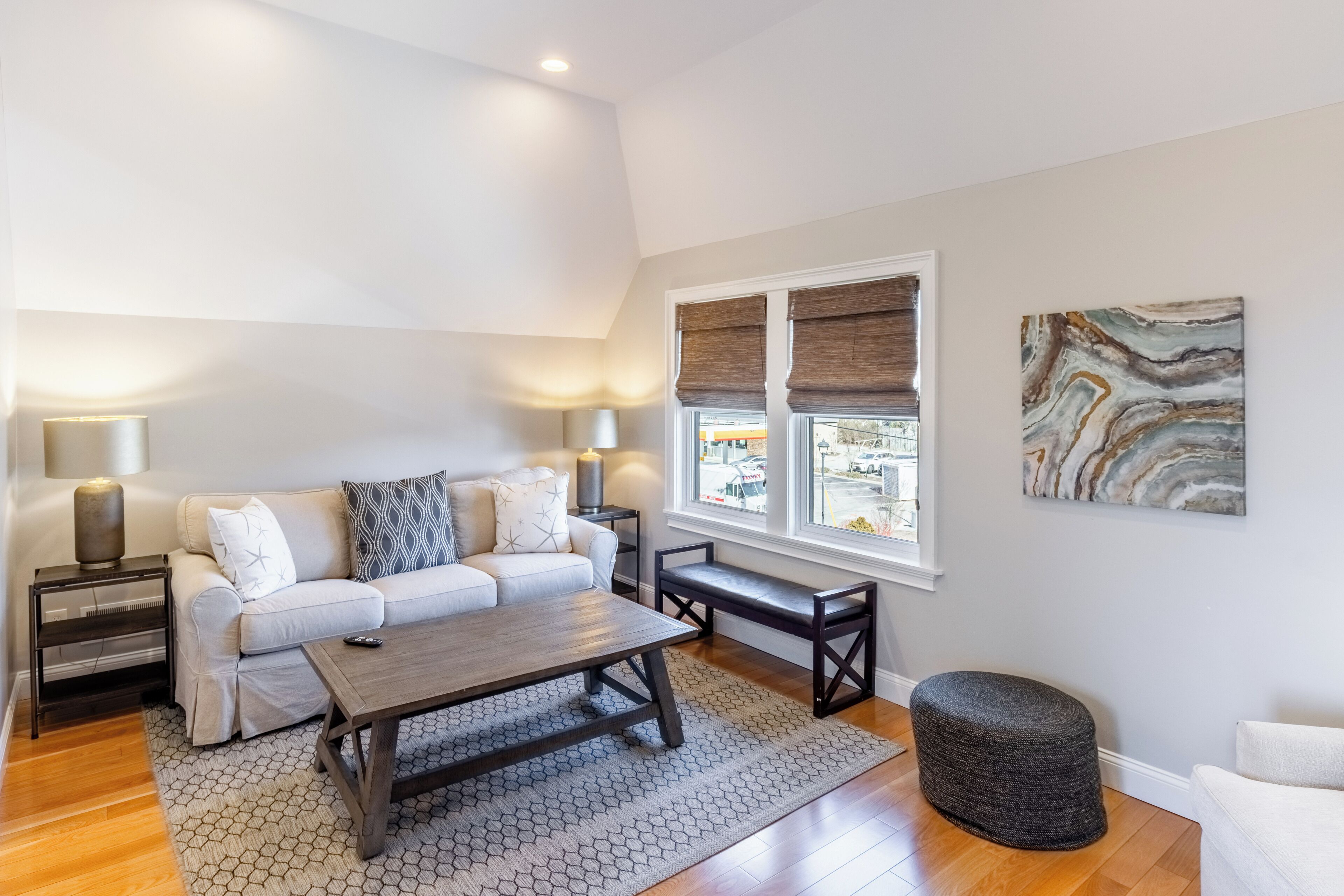 A living room with a sofa, coffee table, and ottoman, a window with blinds, and a painting on the wall.