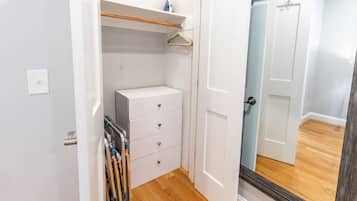 Un pasillo estrecho con una puerta blanca, piso de madera y un mueble blanco con cajones.