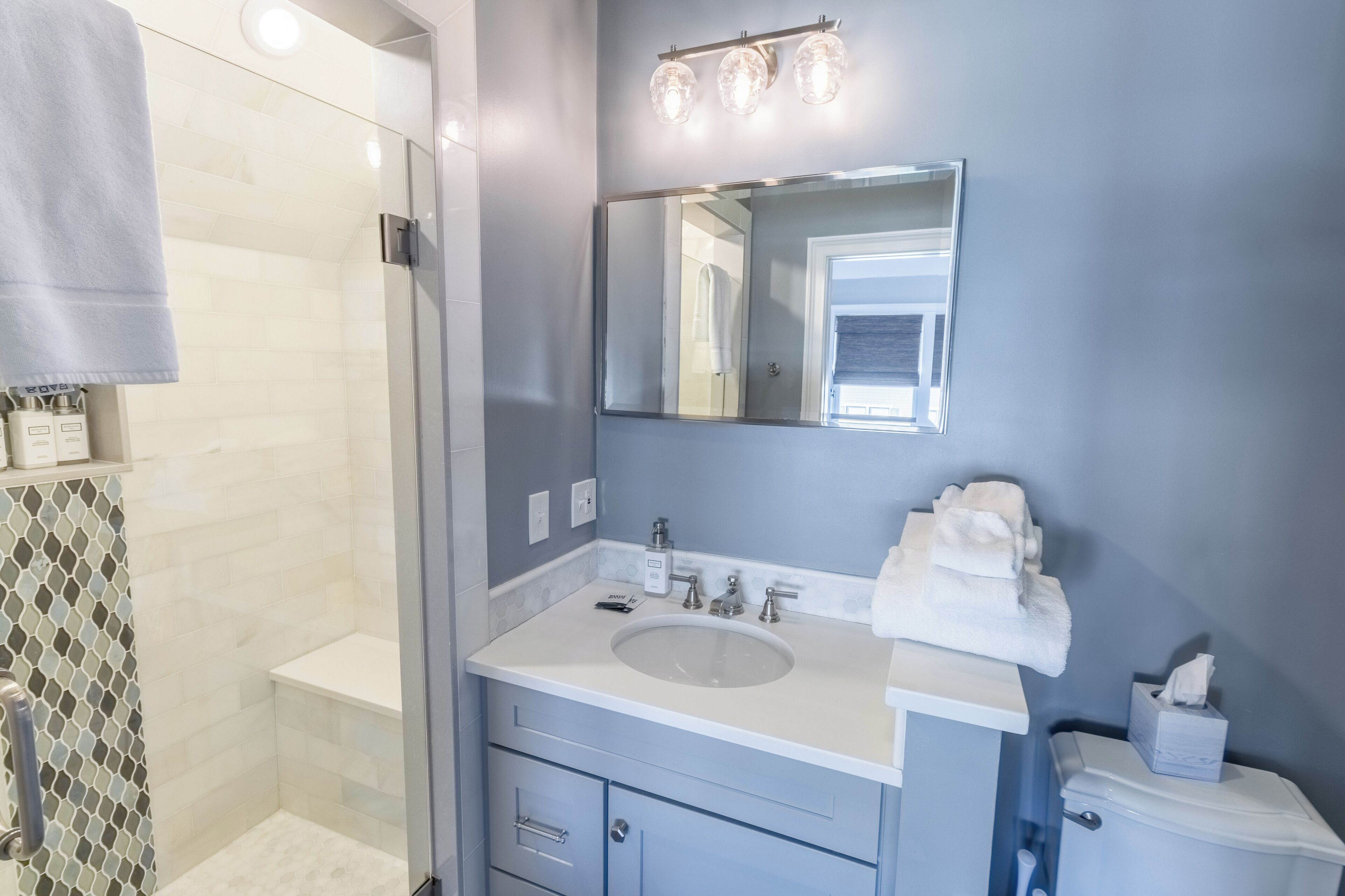 Une salle de bain avec une douche à parois de verre, un lavabo avec un miroir au-dessus et des toilettes.