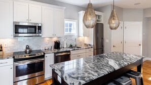 A modern kitchen with white cabinets, stainless steel appliances, a marble island, and pendant lighting. - The Newport Lofts - 595 Thames Street (Newport)