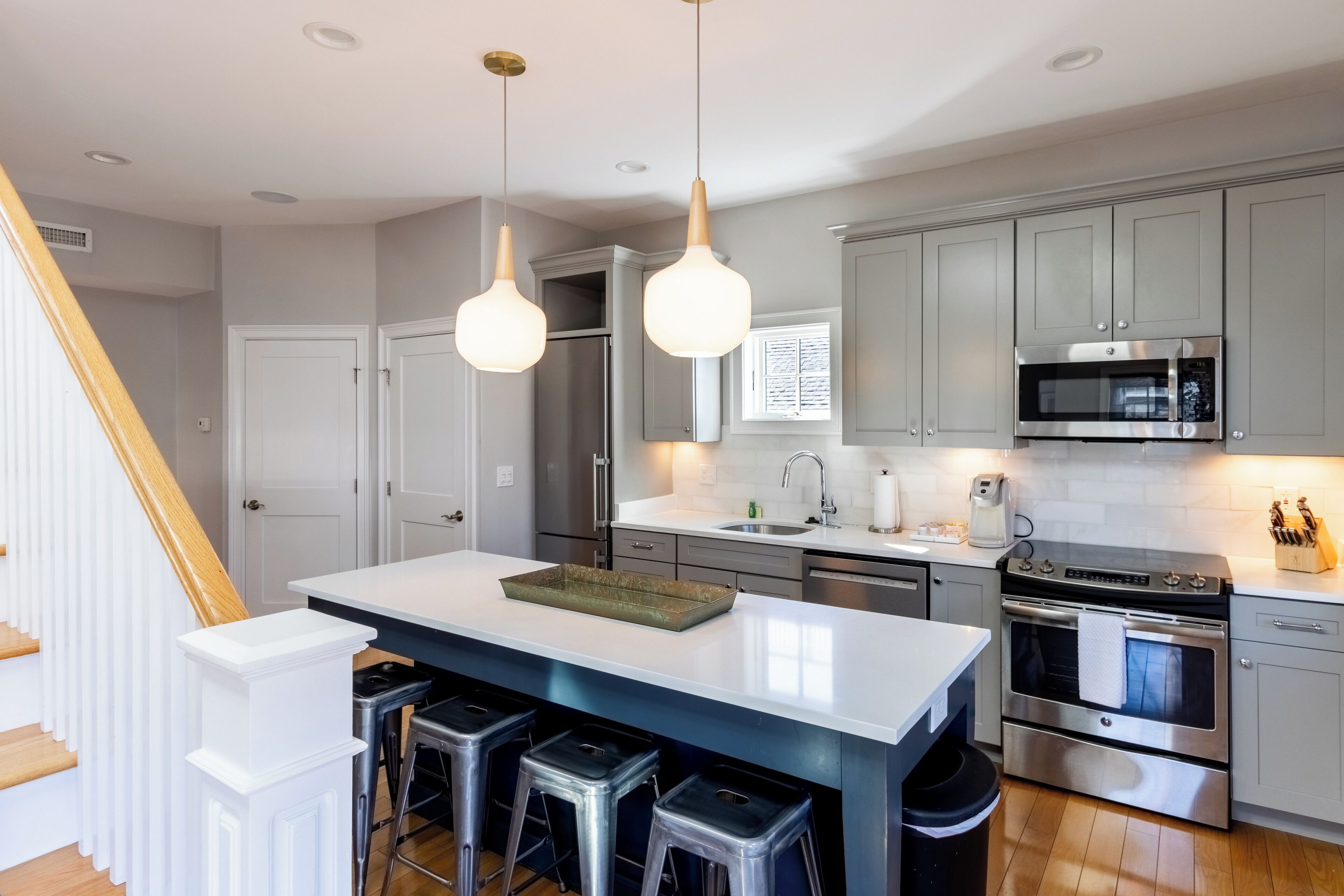 A modern kitchen with grey cabinets, stainless steel appliances, and a central island with stools.
