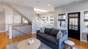 A spacious living room with a grey sofa, a round coffee table, and a staircase leading to another level.