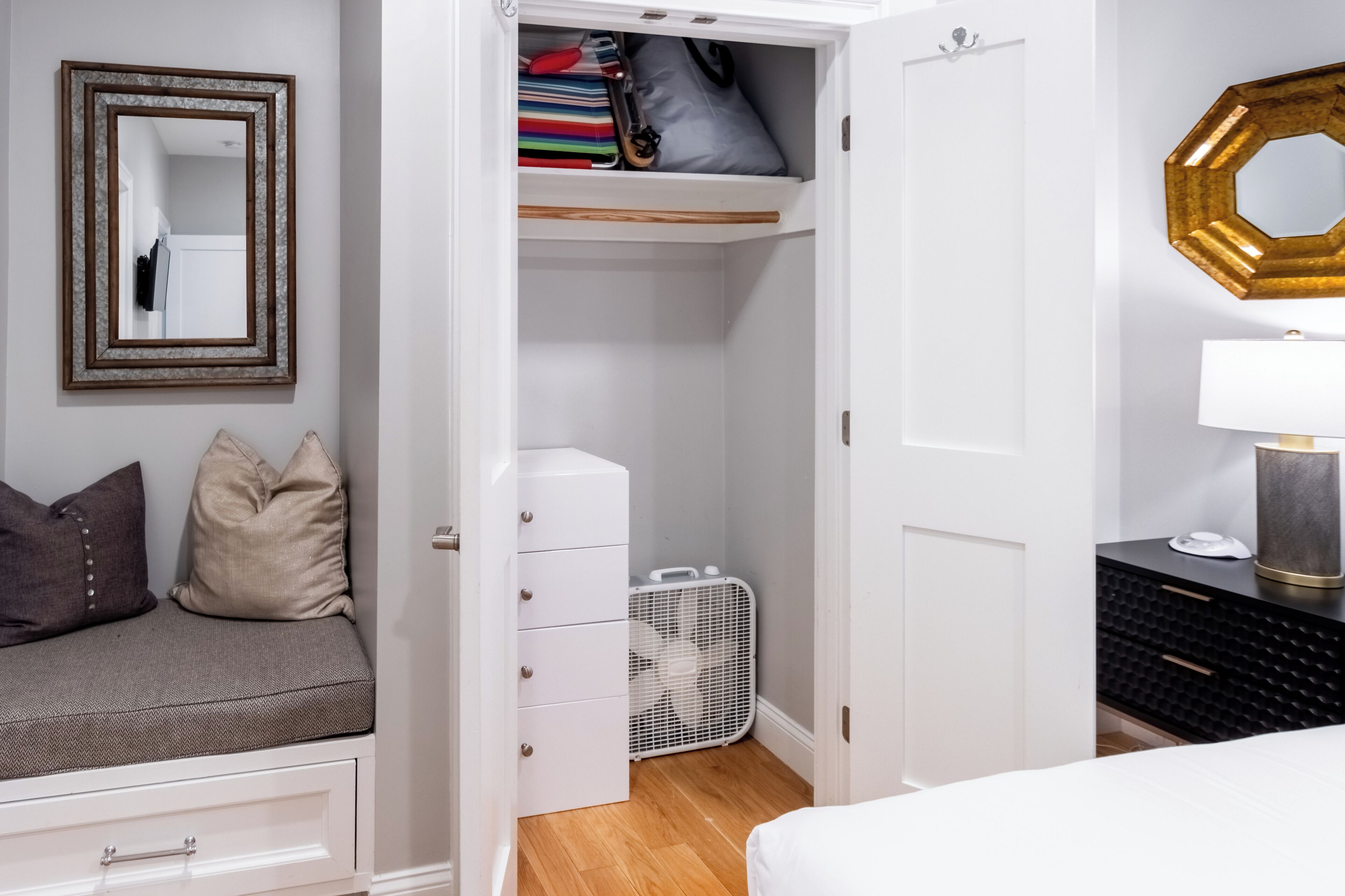 A bedroom with a bed, a dresser, a closet, a mirror, and a bedside table.