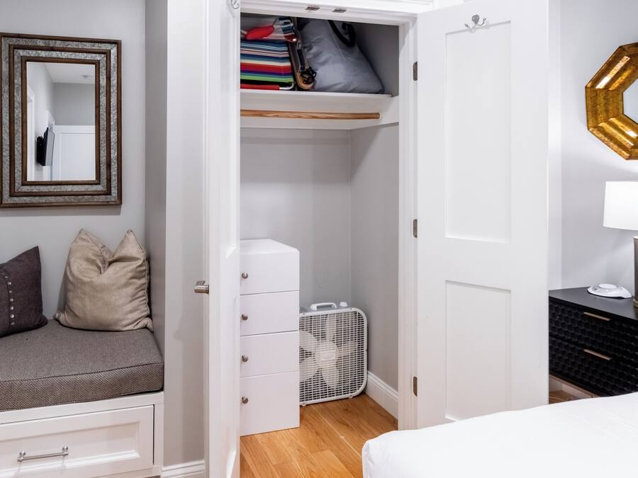 A bedroom with a bed, a dresser, a closet, a mirror, and a bedside table.