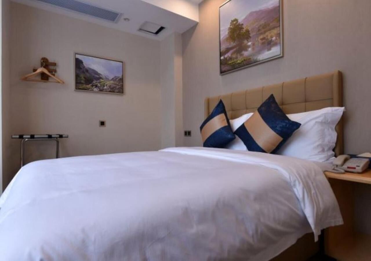 A hotel room with a large bed, a bedside table with a phone, and two paintings on the wall.