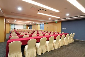 Une salle de conférence avec des rangées de tables et de chaises, équipée de luminaires au plafond et d’un système de ventilation.