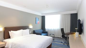 Una habitación de hotel con una cama grande, un escritorio, una silla, un televisor y una ventana con cortinas.