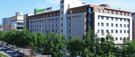 Un immeuble à plusieurs étages, sur lequel on peut voir une grande enseigne « Holiday Inn Express », entouré d’arbres et bordé de voitures garées.
