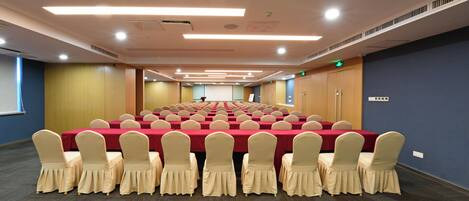 Una sala conferenze con file di tavoli e sedie, dotata di luci a soffitto e uno schermo per proiezioni.