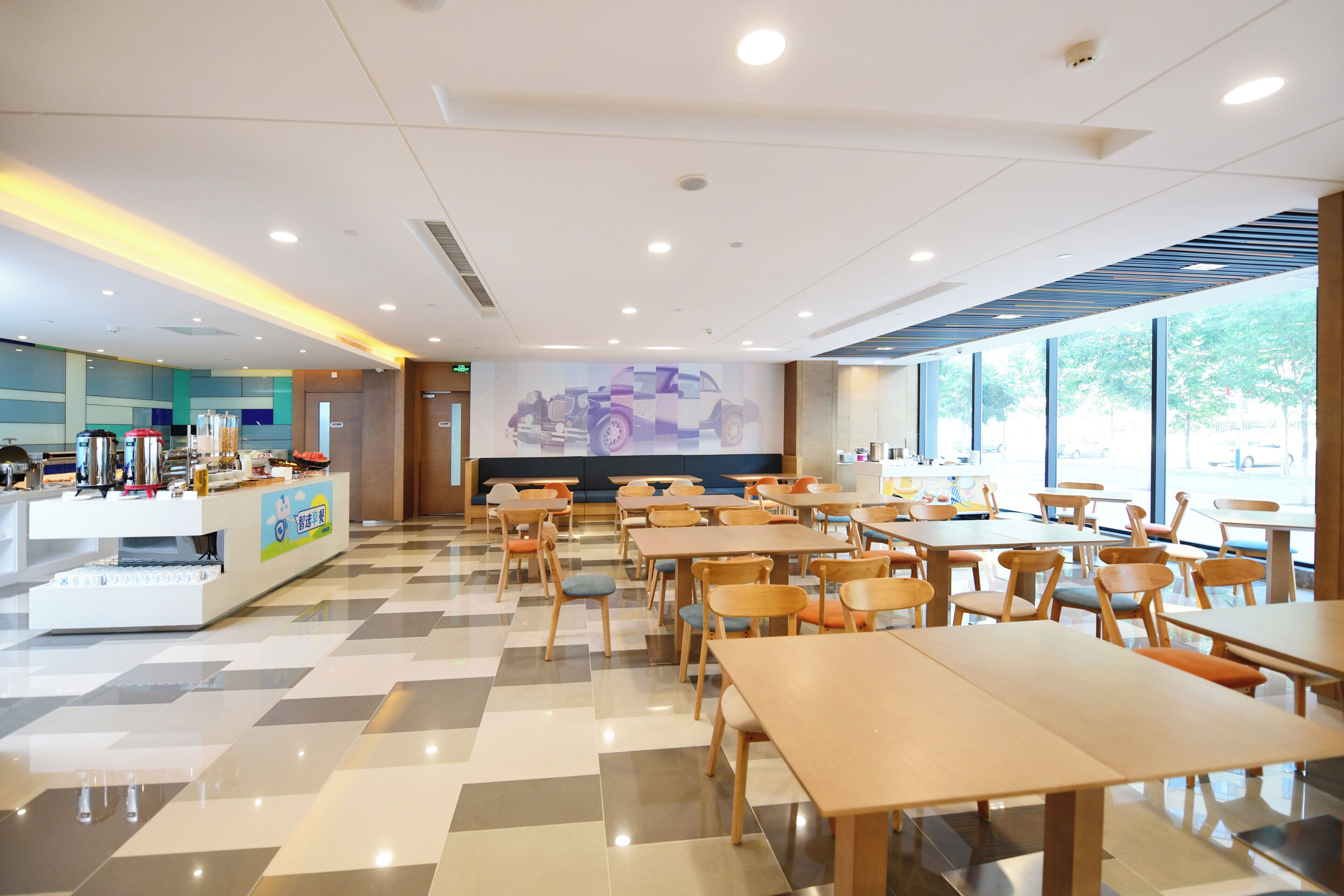 A spacious indoor dining area with multiple tables and chairs, a counter with food items, and a large screen displaying a vehicle.
