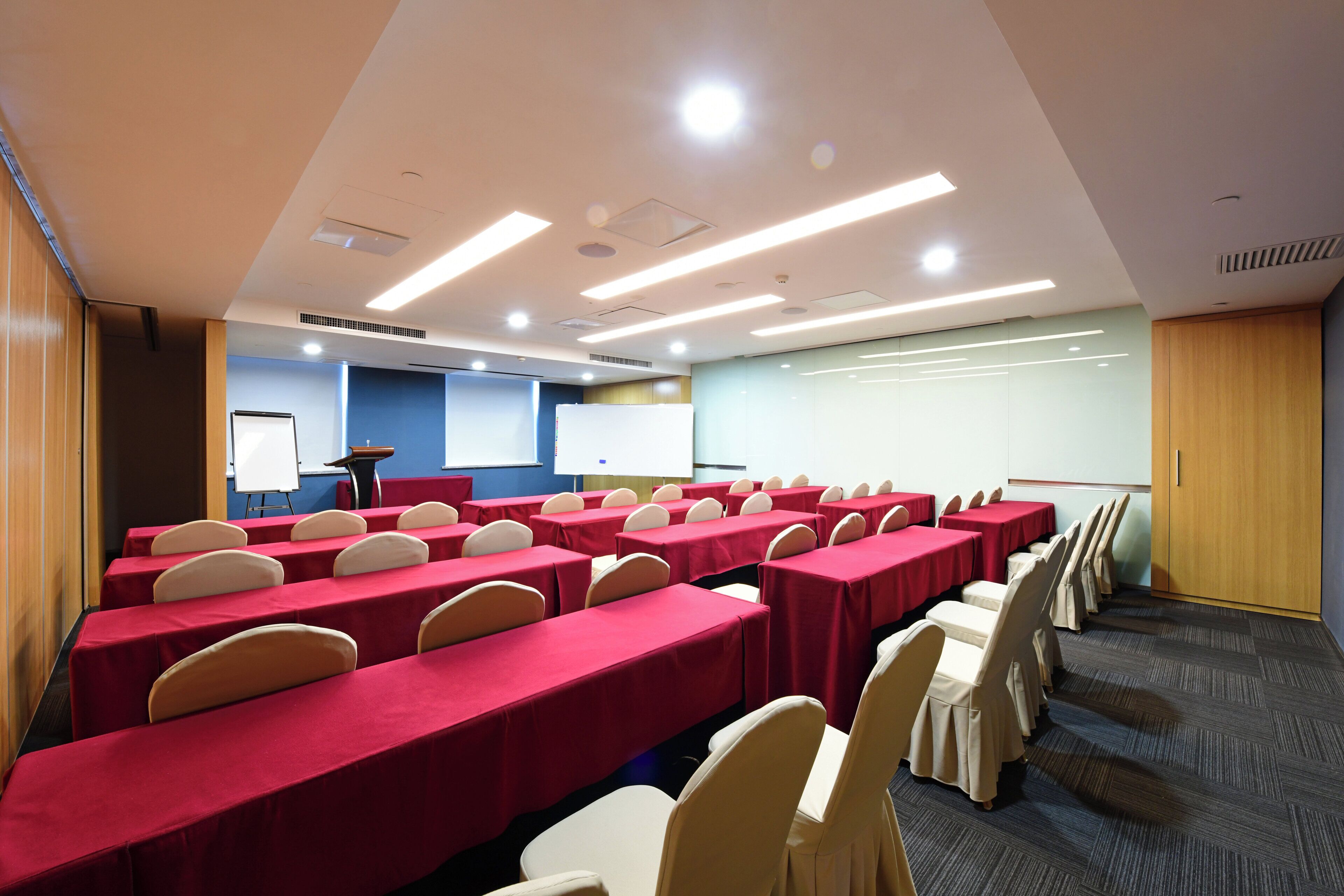 A conference room with rows of tables and chairs, a whiteboard, and a presentation screen.
