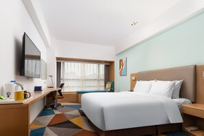 A hotel room with a bed, a desk, a chair, a TV, and a window with curtains.