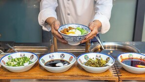 A chef holding a bowl of food with four smaller bowls of condiments in front. - Holiday Inn Express Chengdu Xindu by IHG (Chengdu)