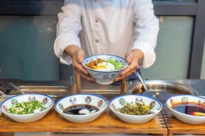 A chef holding a bowl of food with four smaller bowls of condiments in front.