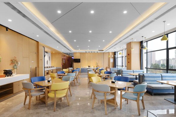Un espace de restauration moderne, doté de plusieurs tables et chaises, de grandes fenêtres et d’un intérieur épuré et bien éclairé.